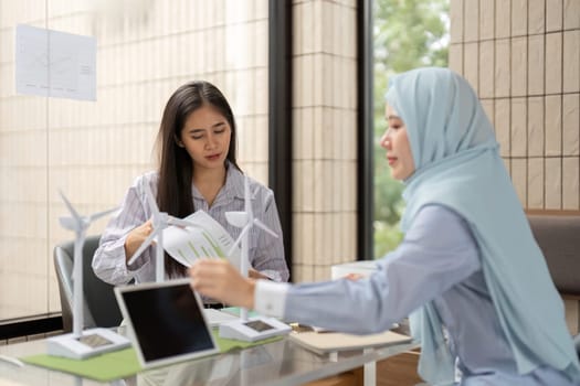 In an inspiring office setting, two professionals engage in discussion about renewable energy technology, showcasing models of wind turbines as part of their eco-innovation strategy.