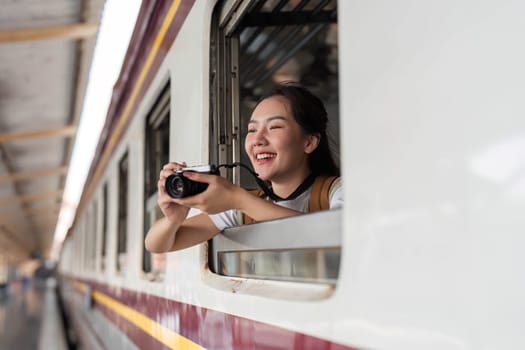 A happy traveler uses her camera to take photos while resting her arms outside the window of a train, embracing the sense of adventure on her trip.