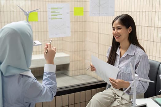 The two women actively brainstorm ideas for sustainable development and ESG solutions, smiling and interacting positively in a modern work environment.