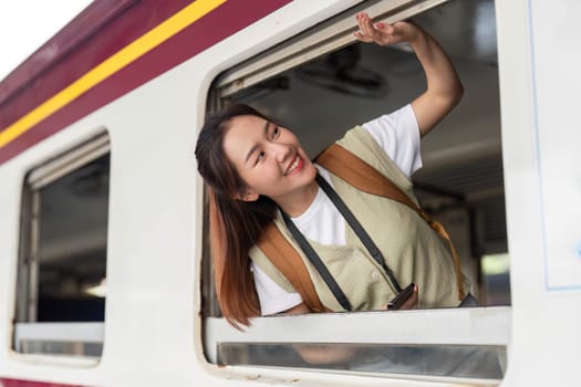 With a playful expression, she enjoys the wind in her hair as she peeks out from the train window, embracing the travel adventure.