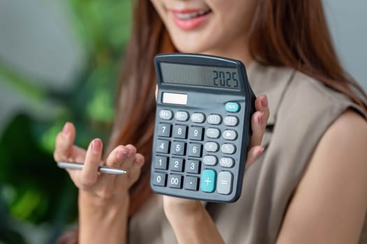 With a smile, a woman shares a calculator showing '2025', symbolizing her optimistic financial projections for the future.