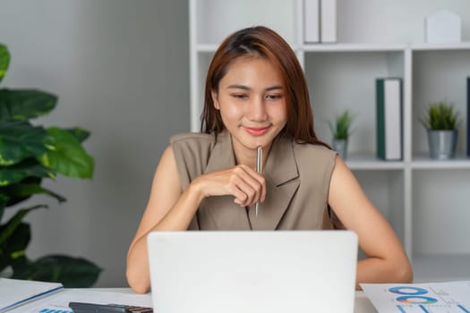 A young professional woman sits at her desk, concentrating on her online tasks. She holds a pen, symbolizing her focus and dedication to her work.