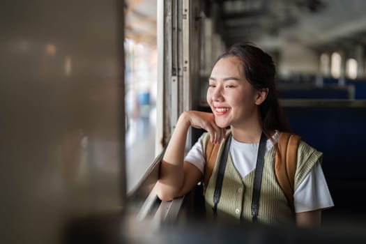 A young woman sits comfortably inside a train, smiling as she reflects on her journey, enjoying the peaceful atmosphere.
