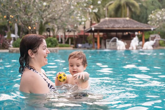 Caucasian woman holds son while swimming in pool on vacation