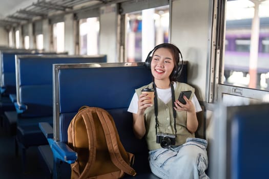 With a cup of coffee in one hand, a young woman sits comfortably on a train, listening to her music and enjoying her traveling experience.