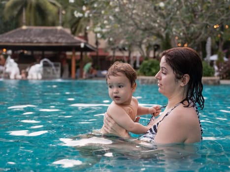 Caucasian woman holds son while swimming in pool on vacation