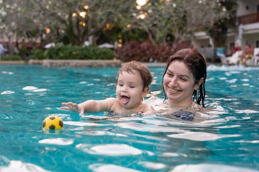 Caucasian woman holds son while swimming in pool on vacation