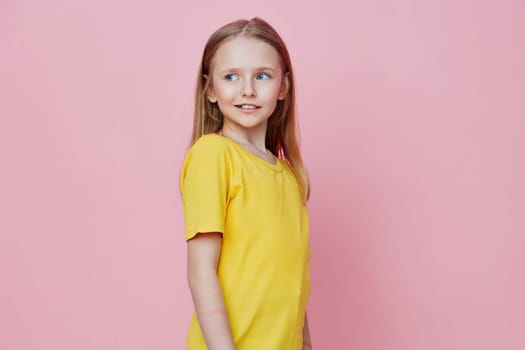 A joyful girl wearing a yellow shirt, standing against a pastel pink background, perfect for themes of childhood, happiness, and vibrant fashion Great for family and lifestyle visuals