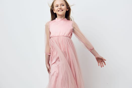 A cheerful young girl dressed in a flowing pink gown with sheer sleeves, exuding happiness in a pastel colored scene, perfect for children s fashion or joyful celebrations