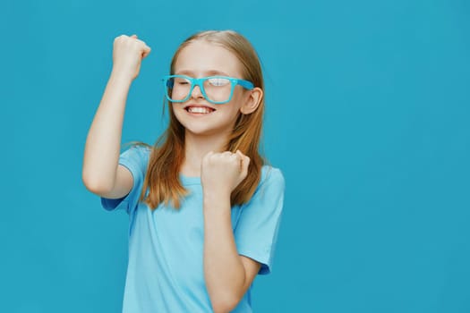 A joyful girl in bright blue glasses celebrating a personal victory, dressed casually in a light blue t shirt, set against a striking turquoise backdrop, representing happiness and youthful energy