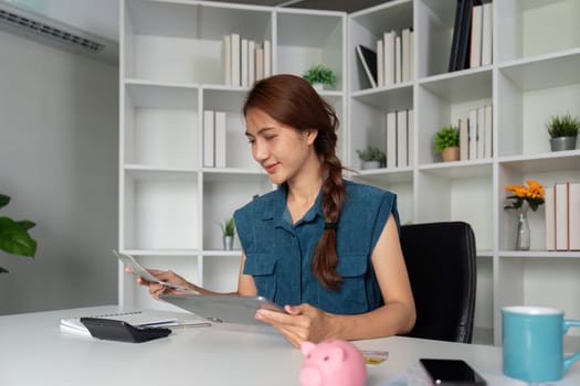 A focused woman examines financial documents at her desk, balancing her budget and planning her finances in a well-organized workspace.