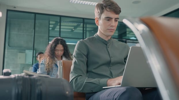 Young handsome man with a suitcase sitting working his laptop at airport terminal hall while waiting landing for her flight, tourist men in international airport, travel trip