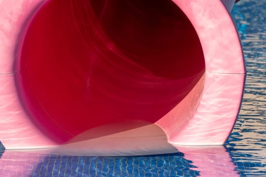 The entrance of a large, bright pink waterslide, with a blue tiled surface below. The slide is partially visible in the background.