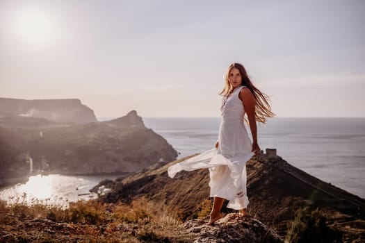 A woman in a white dress stands on a hill overlooking the ocean. The scene is serene and peaceful, with the woman's dress billowing in the wind. The combination of the ocean