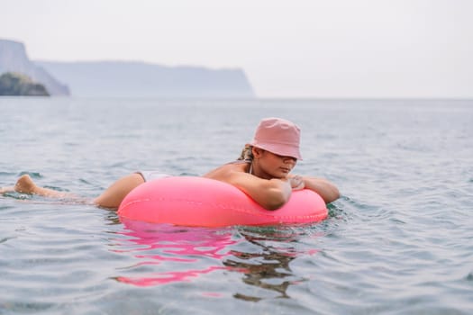 A woman is laying on a pink inflatable raft in the ocean. The scene is peaceful and relaxing, with the woman enjoying the water and the sun