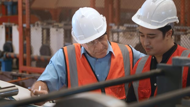 Engineer teaching apprentice to use metal sheet stamping machine, industrial team is working on various projects with tablet computer, worker work together to check the operation system in a factory