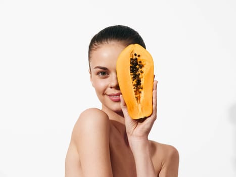 Beautiful young woman with papaya face mask in a spa salon on white background, beauty treatments concept