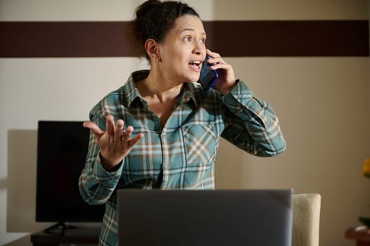 A woman in a home office setting having an engaging conversation on the phone, conveying determination and focus. The room features a laptop and thoughtful interior design, suggesting remote work.