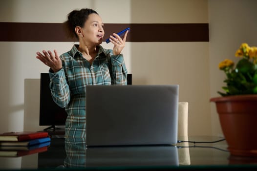 A woman in a home office using technology to communicate. Displaying elements of remote work and multitasking, the image highlights the dynamics of contemporary, tech-driven professional lifestyles.