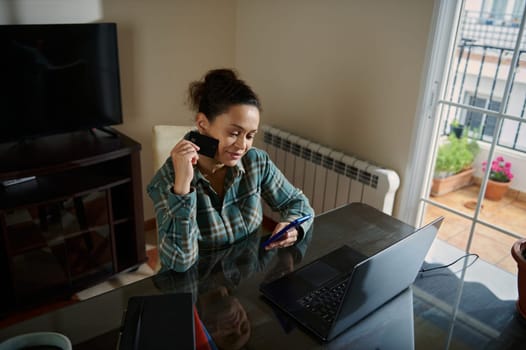 A young lady in a serene home atmosphere shopping online, using her smartphone and holding a credit card. The image captures modern technology usage and online consumer convenience.