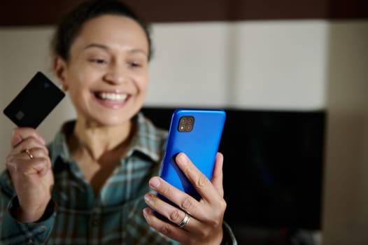 A cheerful woman holds a credit card and a phone, symbolizing online shopping convenience and wireless payments. A moment of joy in using digital technology for banking and purchases.