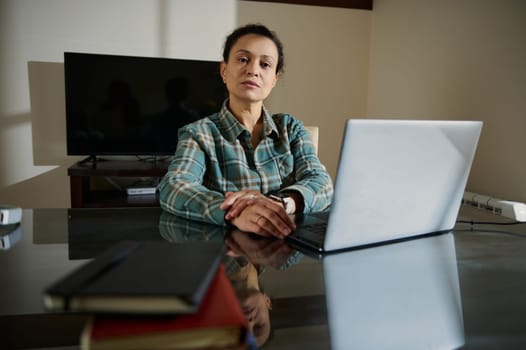 This image shows a confident woman sitting at a desk with a laptop, embodying professionalism, entrepreneurship, and focus in a modern home office environment.
