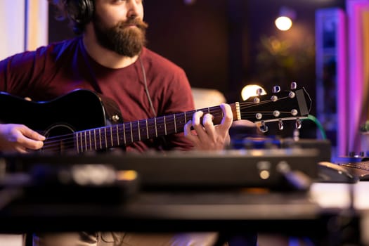 Musician playing guitar and uses mixing gear to create new music, looking at daw software interface on computer. Producer recording soundtracks with electronic equipment, acoustical engineering.