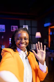 Happy social media star using smartphone camera to capture welcoming intro for vlogging channel. Cheerful influencer excited to connect with loyal audience during livestream, filming in apartment