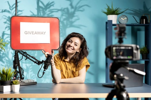 Jolly woman filming sponsored content, holding empty copy space sign, following script while talking to audience. Online star using cardboard bubble speech cutout to do influencer marketing