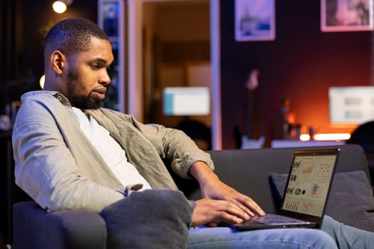 African american specialist working from home using financial graphs analysis, reviewing statistical data to compare supply and demand numbers. Examining business charts on his laptop.