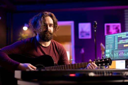 Musician plays acoustic guitar and records melody to compose new song and tunes. Computer screen showing DAW software interface with soundtracks, sound engineer in music production. Camera A.