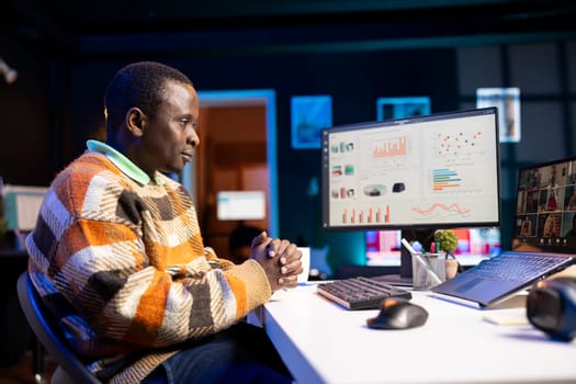 Black man waving on video call and discussing about business infographics, reviewing monthly budget balance and working remotely. Staff focused on conversation during online meeting on pc.