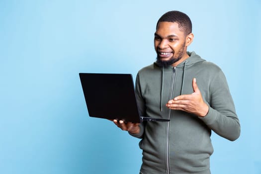 African american person smiling and carefree working on laptop, focused skilled man typing information and browsing online websites. Young adult does paperwork and writes emails.