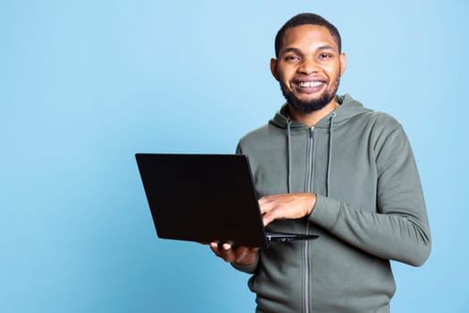 African american man typing on laptop keyboard and checking emails, feeling overjoyed after receiving good news. Employee sending mail online, celebrating after meeting KPIs at work.