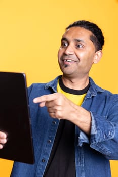 Confident friendly guy meeting with his friends on online web conference, uses his tablet to chat remotely with people. Young indian person having a joyous entertaining conversation.