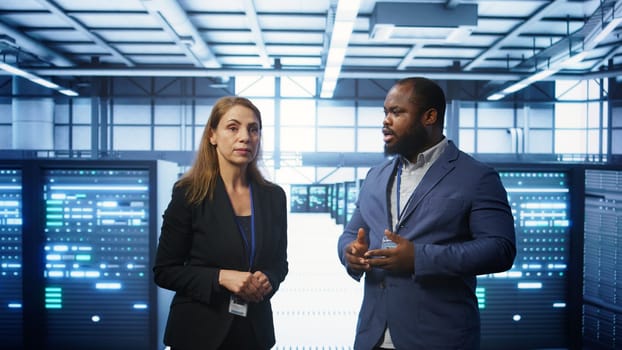 Team of admins in high tech data center looking at hologram visualization. Engineer and coworker working on securing serves using AR tech, preventing hacker attacks, camera B