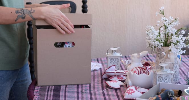 A woman is busy decorating her home for spring, unpacking Easter decorations from a box. She arranges festive items on a table, enhancing the warm atmosphere of springtime.