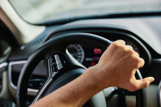 A detailed view of a hand on a steering wheel, showcasing the dashboard and interior elements of a vehicle