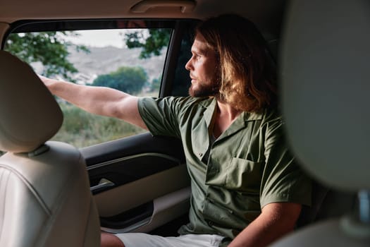 A thoughtful young man in a green shirt gazes out of the car window, enjoying a peaceful moment in the countryside