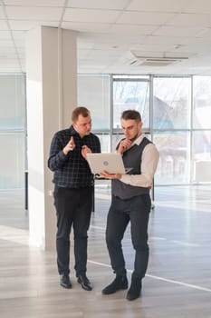 Two Caucasian men looking at a laptop and discussing work