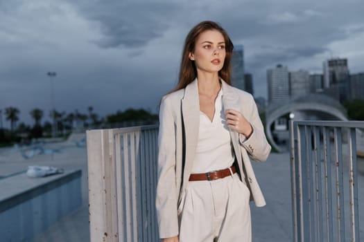 A confident woman in a stylish suit stands in an urban environment, showcasing professionalism and strength. The cloudy sky adds a dramatic touch to her powerful presence.