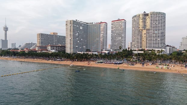 Bustling beachside cityscape featuring high rise buildings along a sandy shoreline with people enjoying the beach and water activities under a partly cloudy sky