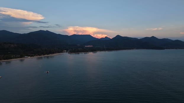 Tranquil coastal scenery featuring calm waters, lush mountains, and a vibrant sunset sky. The peaceful shoreline invites relaxation and contemplation, highlighting nature's beauty