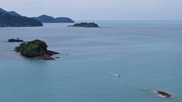 Motorboat is navigating the calm turquoise waters of the sea near tropical islands covered in lush vegetation, creating a serene and idyllic scene