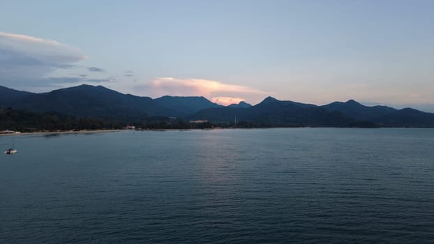 Calm ocean waters reflecting the warm hues of sunset light, framed by majestic mountains and a pristine beach, creating a tranquil and serene atmosphere perfect for relaxation