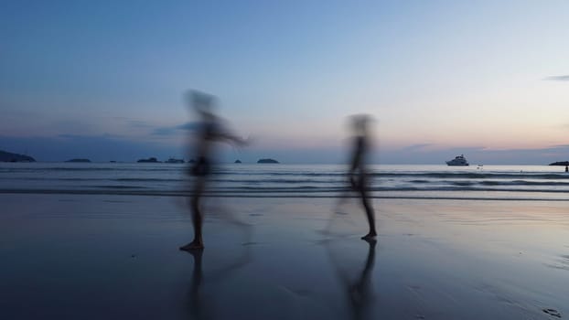 Two tourists are running along the beach at dusk, their figures blurred by motion, with a boat visible in the distance and the sky reflecting in the wet sand