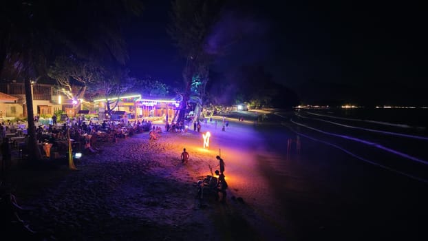 Dining tourists enjoying a mesmerizing fire show at a beach restaurant under the night sky, creating a vibrant and festive atmosphere filled with excitement and tropical charm
