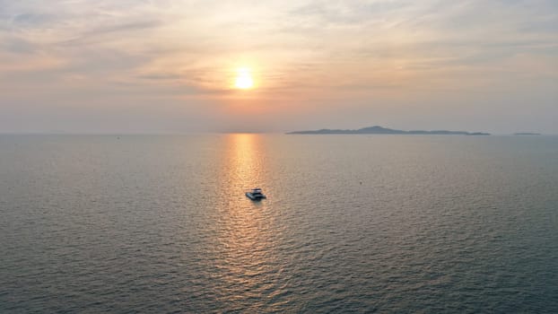 Golden sun setting over a tranquil ocean, casting a warm glow on the water as a catamaran sails peacefully towards the horizon, with a distant island adding to the serene seascape