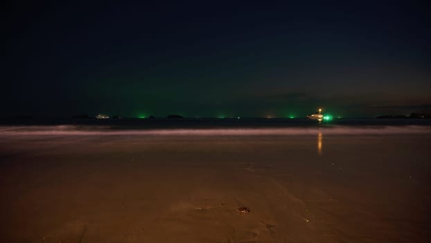 Long exposure capturing fishing boats glowing with green light on a tranquil sea, with a sandy beach in the foreground under the night sky, creating a serene and picturesque scene