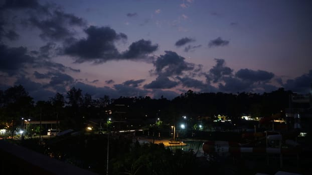 Streetlights casting a warm glow over a deserted water park at dusk, highlighting dramatic clouds and vibrant sunset colors painting the sky, creating a serene evening atmosphere